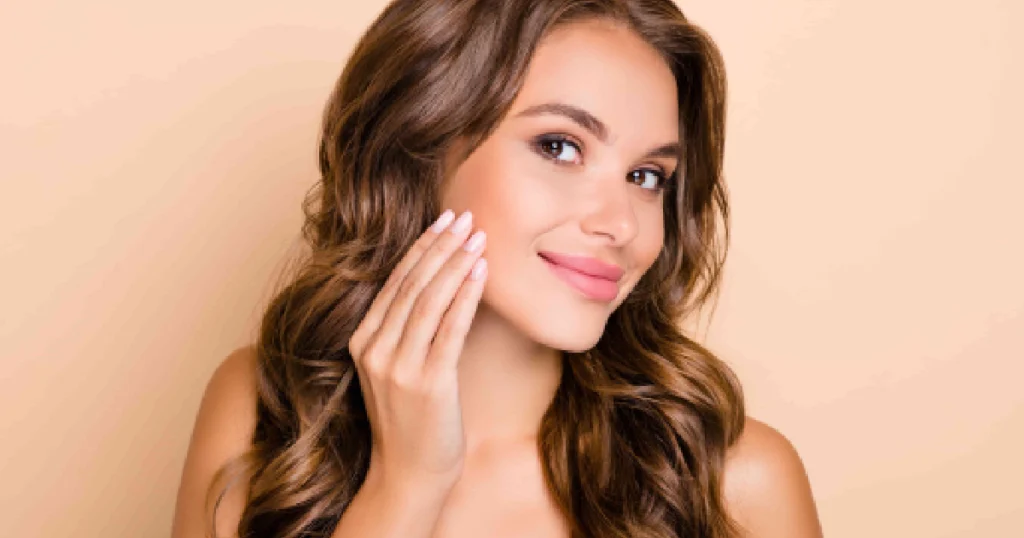 Smiling woman with smooth radiant skin touching her cheek, showing results of MOXI By Sciton in Sidney, NE for sun damage and skin rejuvenation.