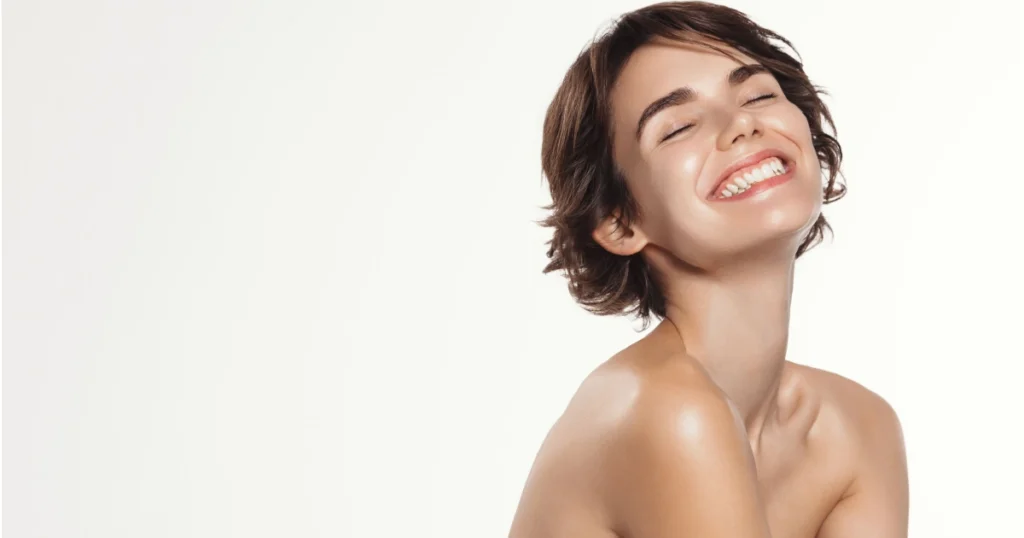 A young woman with short brown hair, smiling with eyes closed, showing radiant, healthy skin after Peptide Therapy in Sidney, NE.